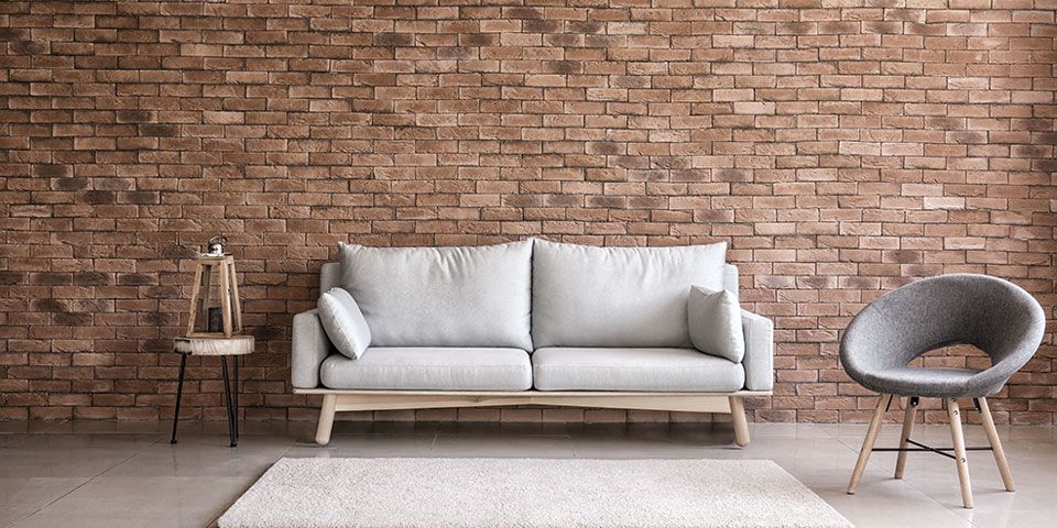 Modern living room with a gray sofa, brick wall, minimalist decor, and a gray chair.