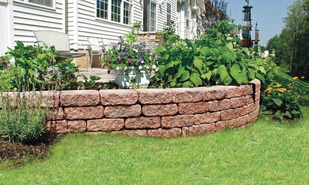 Curved stone retaining wall with vibrant garden and patio seating in a backyard setting.