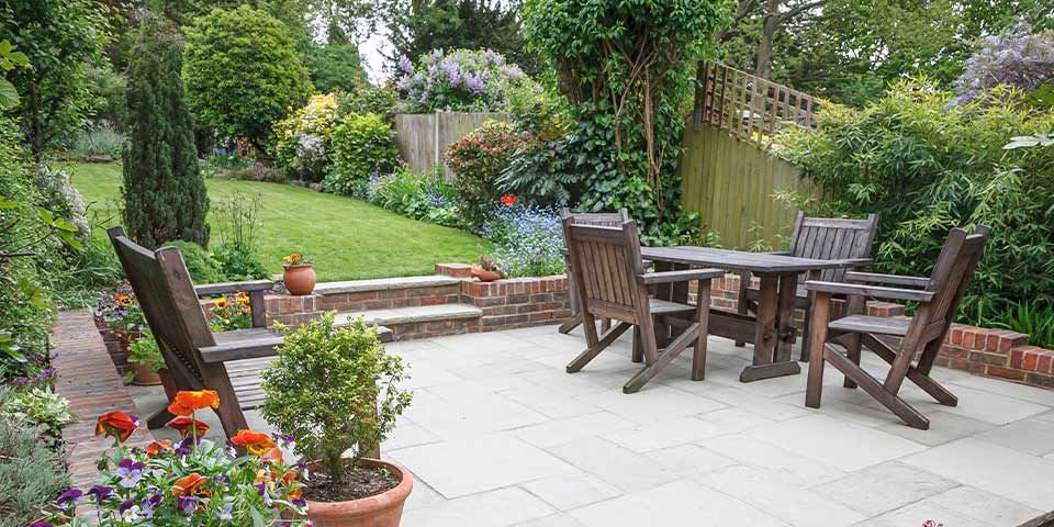 Lush garden patio with wooden furniture, vibrant flowers, and green trees, perfect for outdoor relaxation and gatherings.