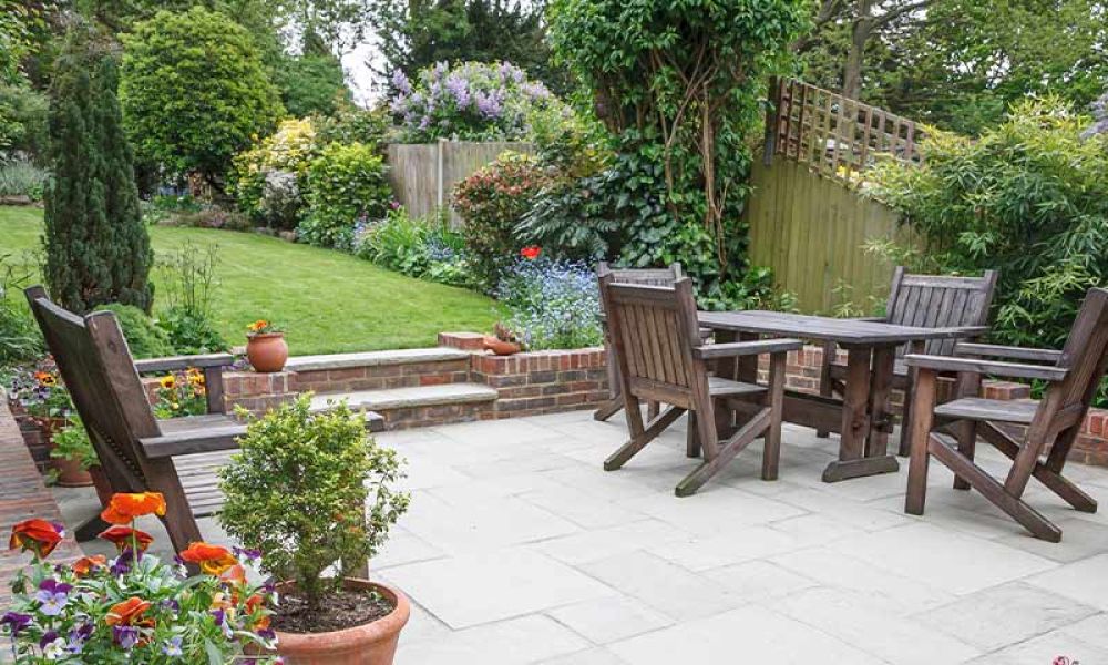 Lush garden patio with wooden furniture, vibrant flowers, and green trees, perfect for outdoor relaxation and gatherings.