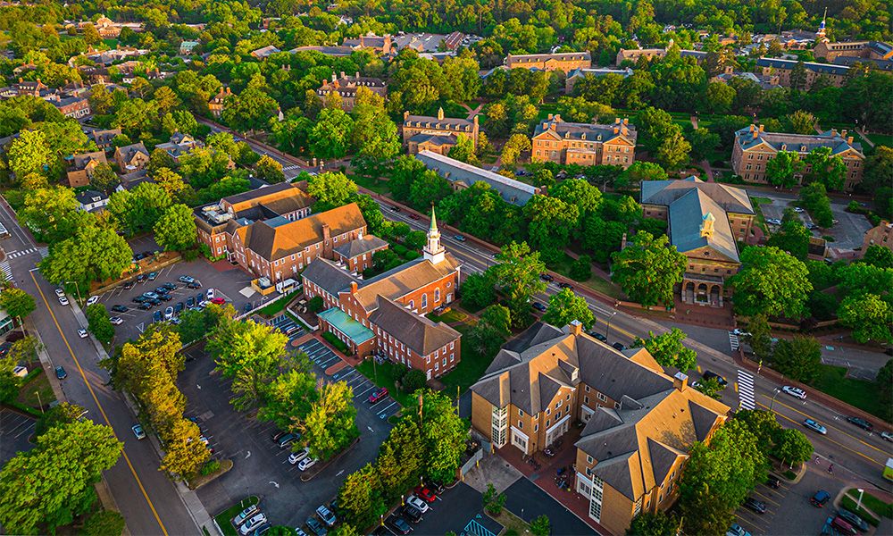 Aerial view of a picturesque college campus with historic buildings amidst lush green trees and scenic pathways.