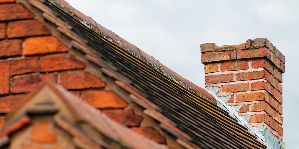 Brick chimney atop a sloped red-tiled roof against a cloudy sky, showcasing traditional architectural design.