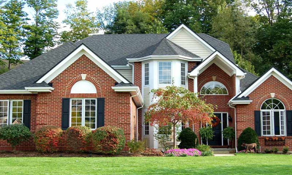 Beautiful brick house with large windows, surrounded by lush greenery and a well-maintained lawn.