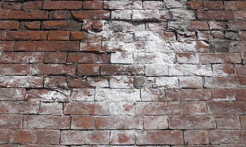 Old brick wall with white textured patches, showing weathered and worn bricks in a rustic pattern.