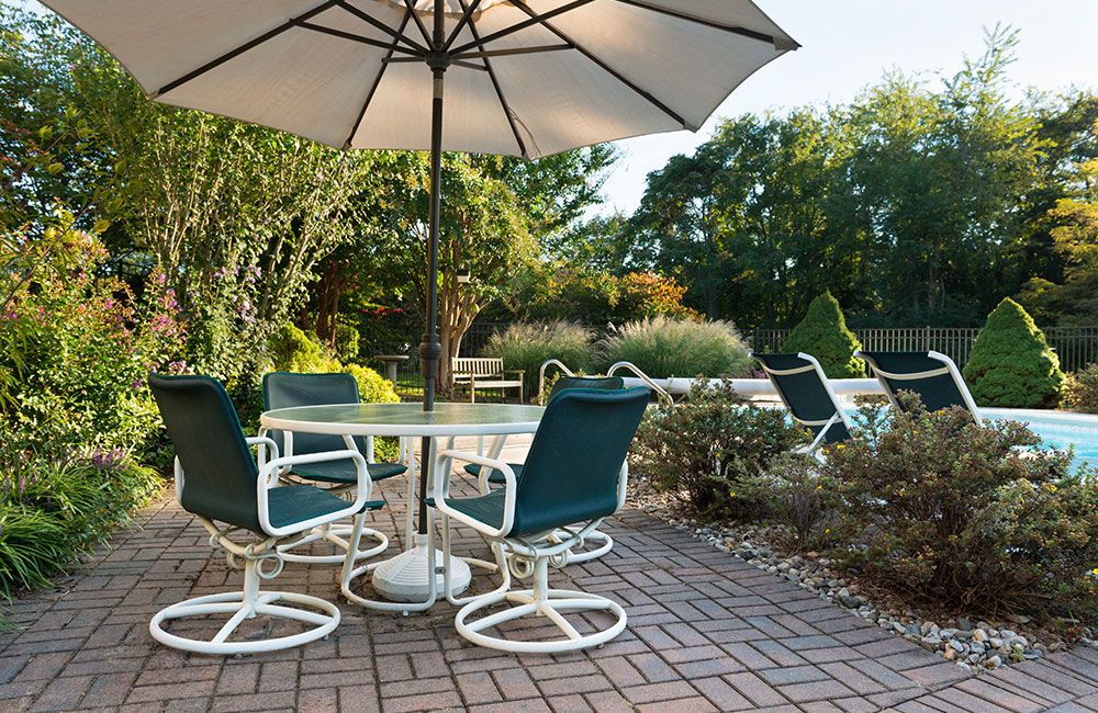 Poolside patio with umbrella, chairs, and greenery on a sunny day. Ideal for outdoor relaxation and gatherings.