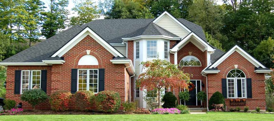 Beautiful brick house with large windows, surrounded by lush greenery and a well-maintained lawn.