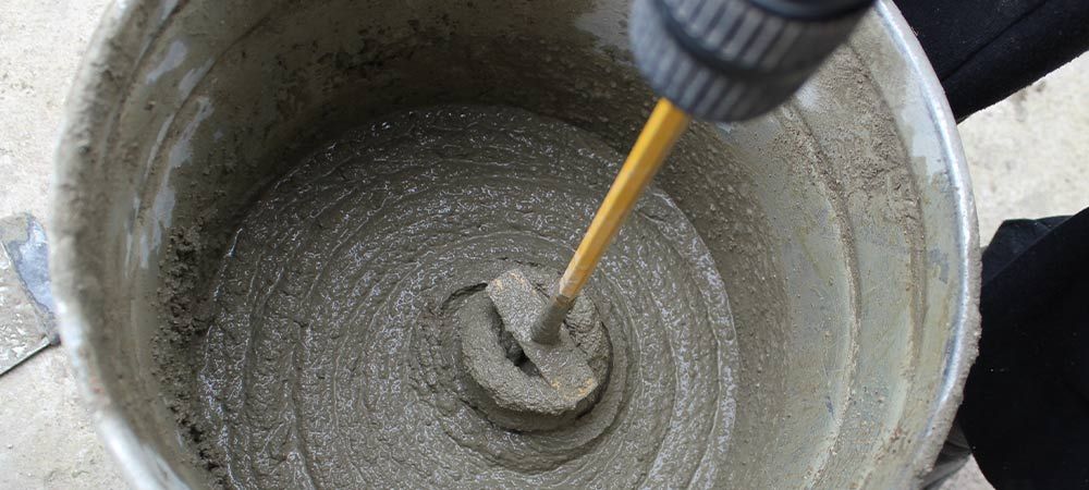 Mixing cement with a drill in a bucket: DIY home improvement, construction materials, and concrete preparation.