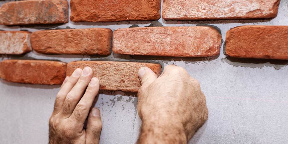 Hands installing red brick veneer on a wall for home construction or renovation.