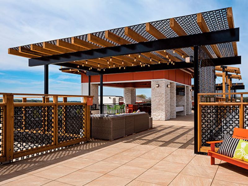 Rooftop patio with wooden pergola, modern outdoor seating, and decorative railing. The area features a bar counter and a view of the sky, creating a stylish and inviting space for relaxation.