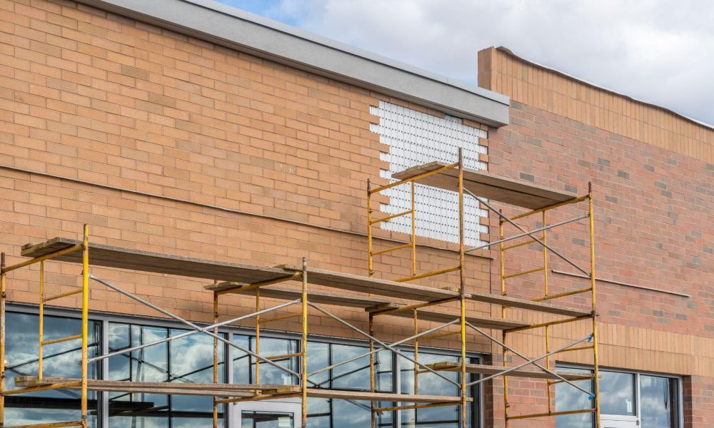 Construction scaffolding on a brick building facade under renovation against a cloudy sky.