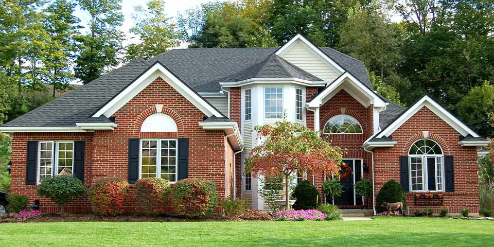 Beautiful brick house with large windows, surrounded by lush greenery and a well-maintained lawn.