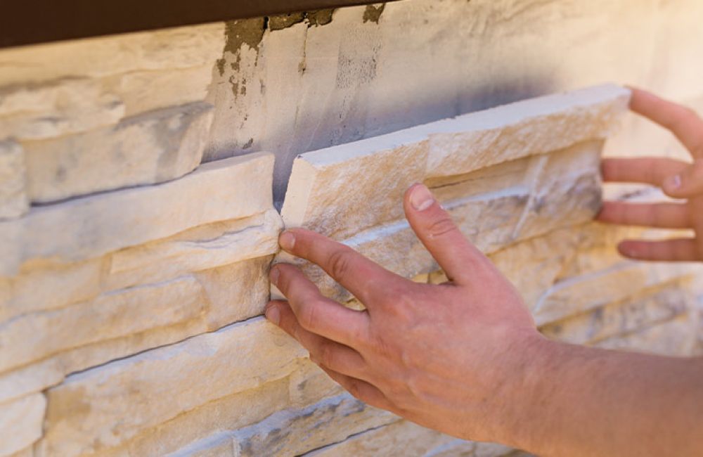 Hands placing stone veneer on exterior wall for home improvement.