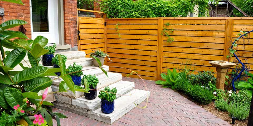 Cozy backyard patio with stone steps, potted plants, wooden fence, and lush greenery for a serene outdoor retreat.