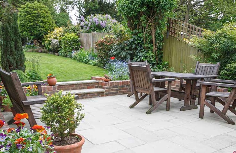 Lush garden patio with wooden furniture, vibrant flowers, and green trees, perfect for outdoor relaxation and gatherings.