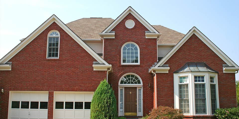 Red brick suburban house with large bay window and an elegant arched entryway on a sunny day.