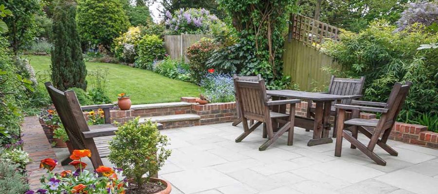 Lush garden patio with wooden furniture, vibrant flowers, and green trees, perfect for outdoor relaxation and gatherings.