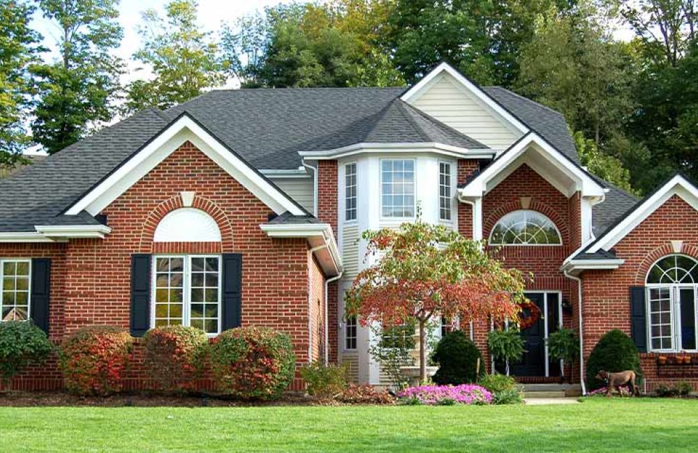 Beautiful brick house with large windows, surrounded by lush greenery and a well-maintained lawn.