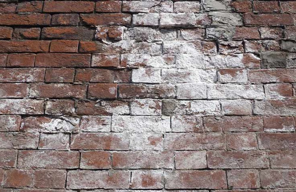 Old brick wall with white textured patches, showing weathered and worn bricks in a rustic pattern.