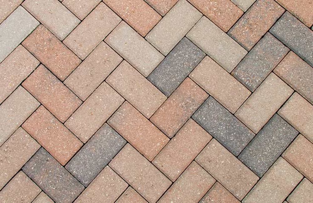 Herringbone pattern of interlocking paver bricks in earthy tones for outdoor flooring and landscaping design.