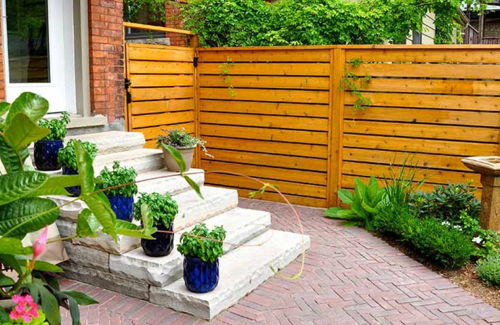 Cozy backyard patio with stone steps, potted plants, wooden fence, and lush greenery for a serene outdoor retreat.