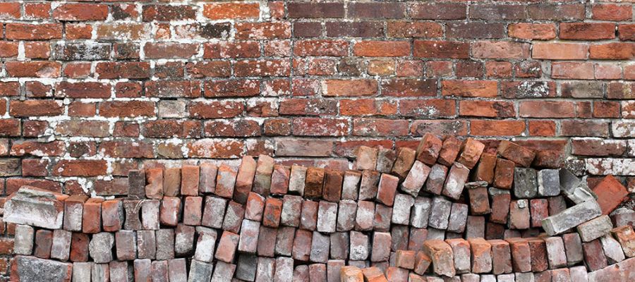 Old brick wall with moss and uneven bricks, showcasing rustic texture and vintage architecture.