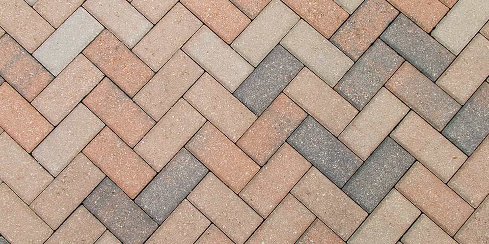 Herringbone pattern of interlocking paver bricks in earthy tones for outdoor flooring and landscaping design.