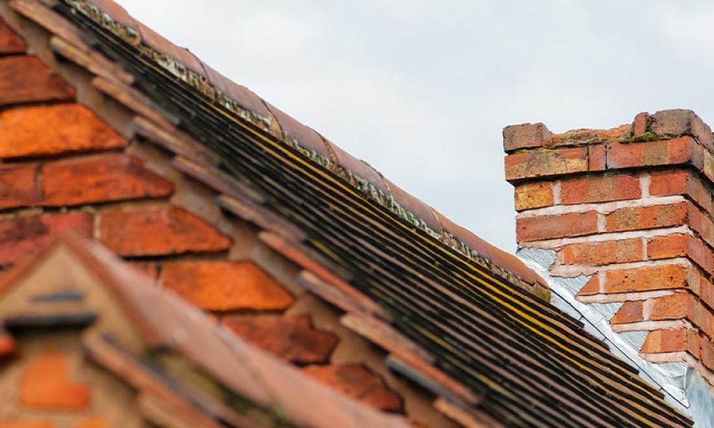 Brick chimney atop a sloped red-tiled roof against a cloudy sky, showcasing traditional architectural design.