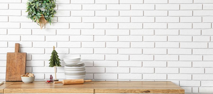 Kitchen counter with cutting boards, dishes, and a wreath against a white brick wall for a cozy holiday vibe.