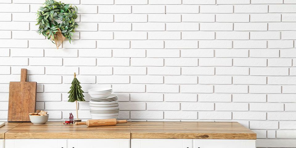 Kitchen counter with cutting boards, dishes, and a wreath against a white brick wall for a cozy holiday vibe.