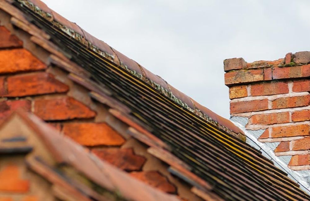 Brick chimney atop a sloped red-tiled roof against a cloudy sky, showcasing traditional architectural design.