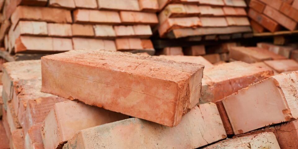 A stack of red construction bricks piled haphazardly in a construction site setting.