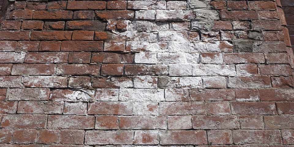 Old brick wall with white textured patches, showing weathered and worn bricks in a rustic pattern.
