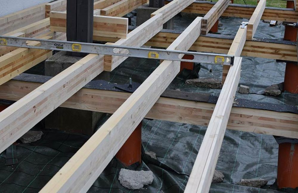 Building a wooden deck foundation with beams and level tool for precise alignment on construction site.
