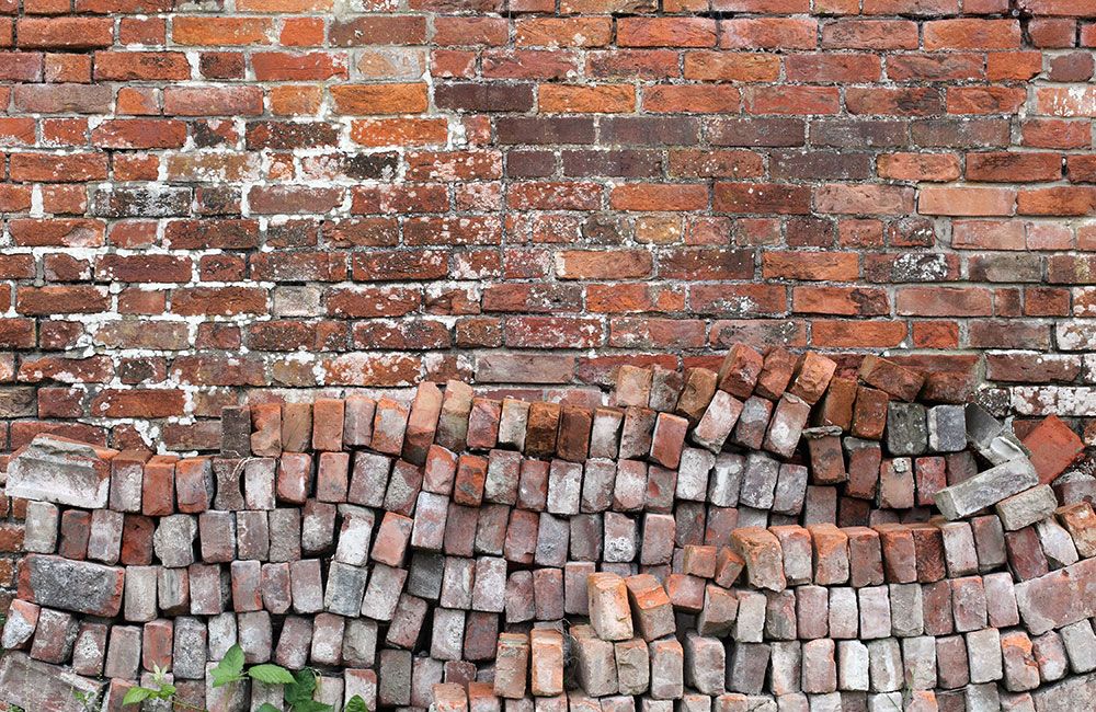 Old brick wall with moss and uneven bricks, showcasing rustic texture and vintage architecture.