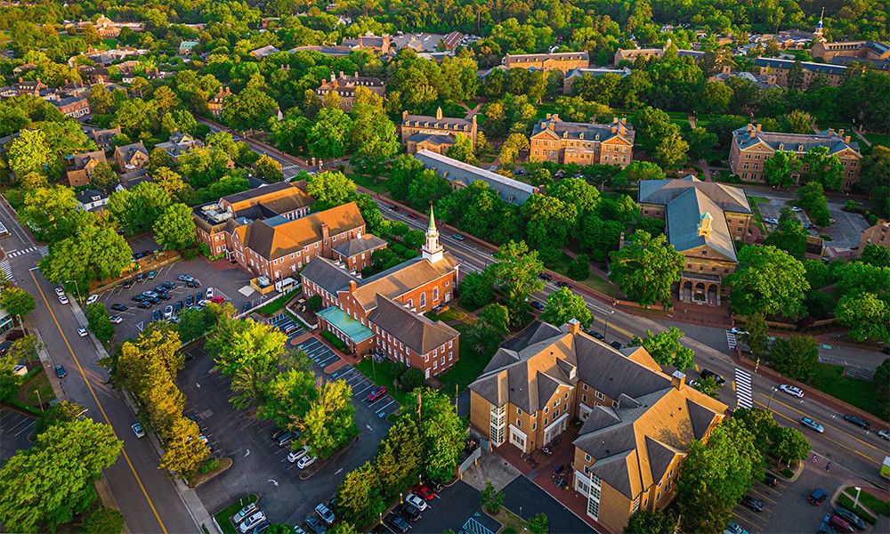 Aerial view of a picturesque college campus with historic buildings amidst lush green trees and scenic pathways.