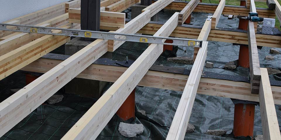 Building a wooden deck foundation with beams and level tool for precise alignment on construction site.
