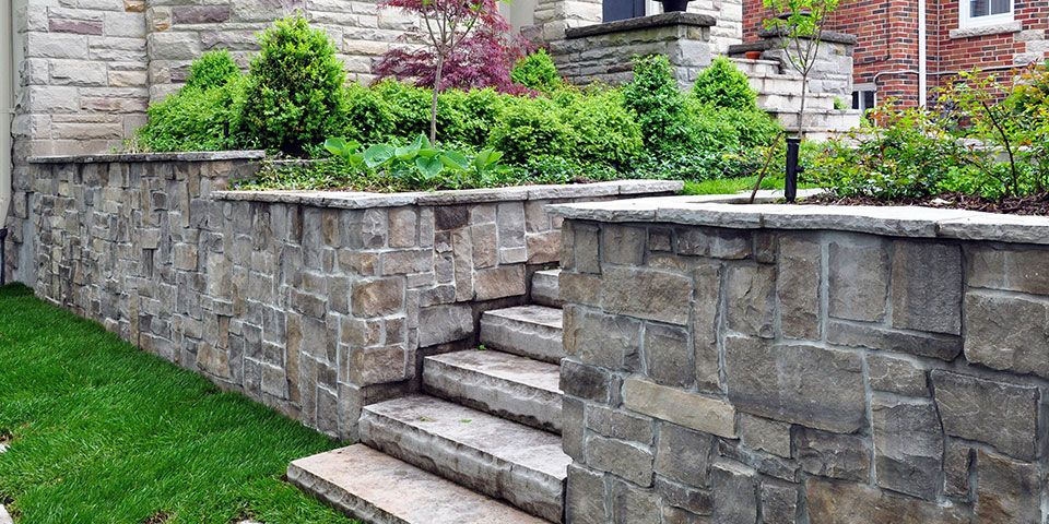 Stone retaining wall with steps and lush greenery in a landscaped garden setting, enhancing curb appeal.