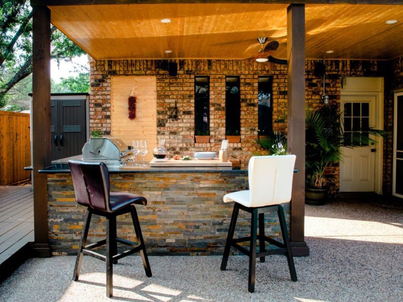 Outdoor kitchen with stone bar, two chairs, grill, and wooden ceiling, enhancing patio for entertaining and dining.