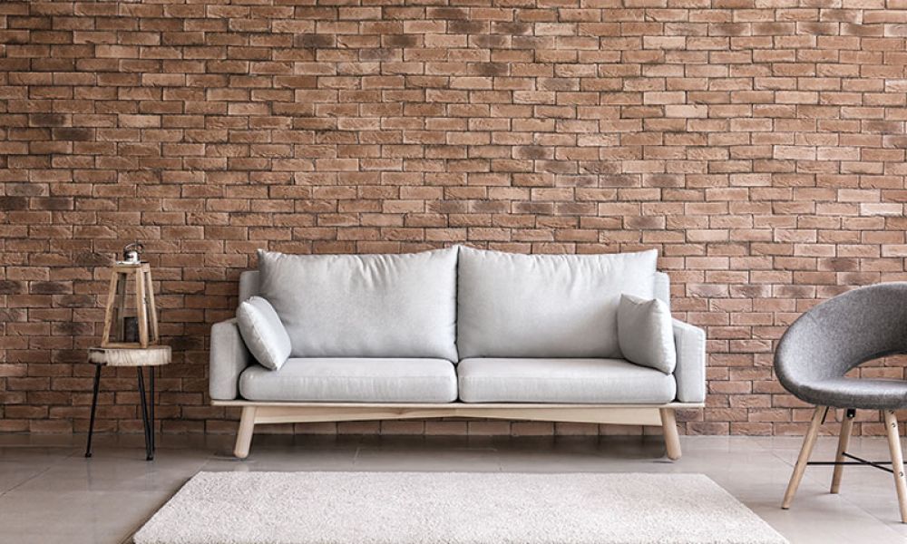 Modern living room with a gray sofa, brick wall, minimalist decor, and a gray chair.
