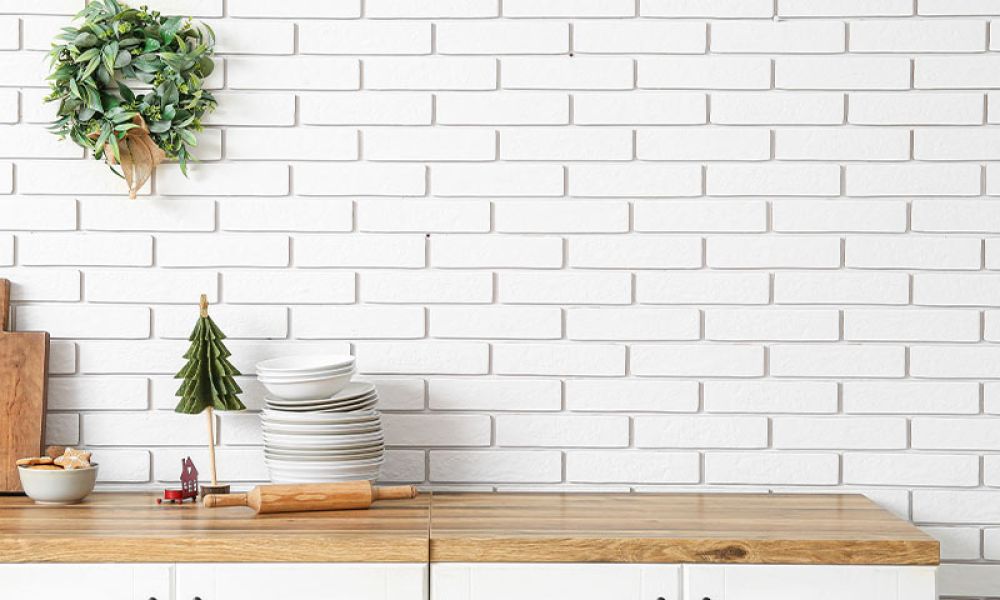 Kitchen counter with cutting boards, dishes, and a wreath against a white brick wall for a cozy holiday vibe.