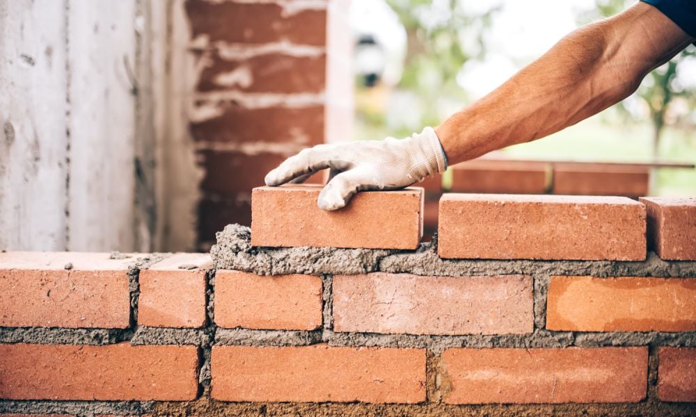 bricklayer worker placing bricks on cement while building exterior walls