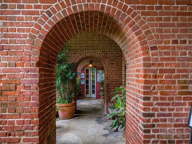 Brick archway hallway with potted plants and a sign on the side. Doorway visible at the end.