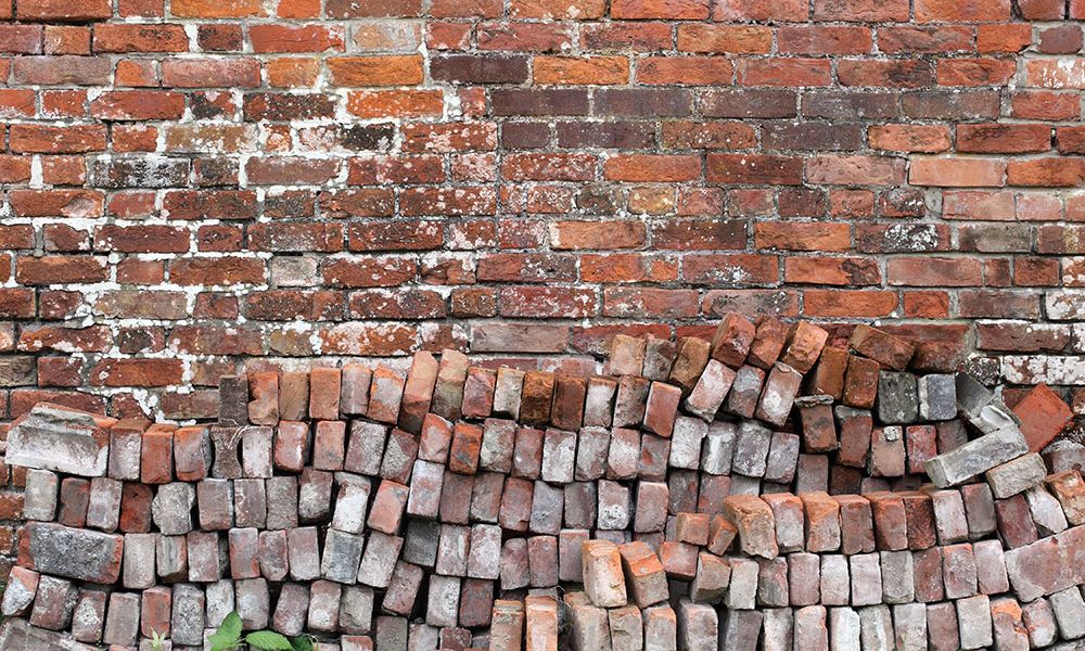 Old brick wall with moss and uneven bricks, showcasing rustic texture and vintage architecture.
