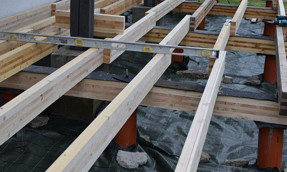 Building a wooden deck foundation with beams and level tool for precise alignment on construction site.
