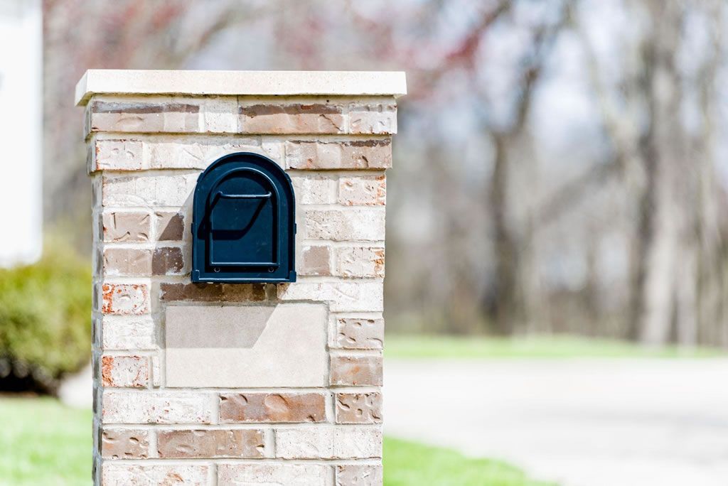 Black mailbox on a brick pillar in a suburban neighborhood.