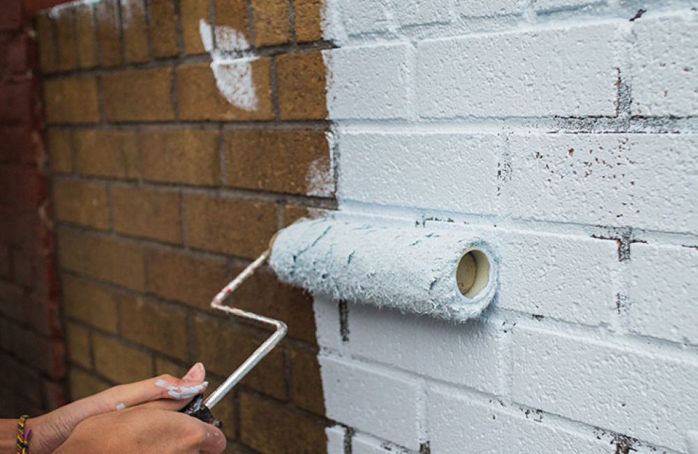 man painting a brick wall white