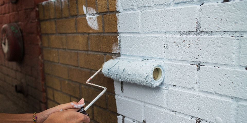 man painting a brick wall white