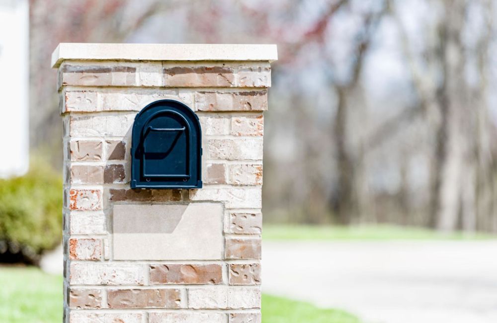 Black mailbox on a brick pillar in a suburban neighborhood.