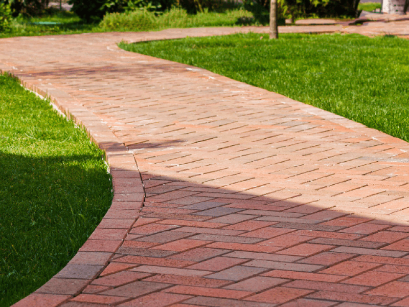 Curved brick pathway with green grass on both sides, leading through a garden landscape.