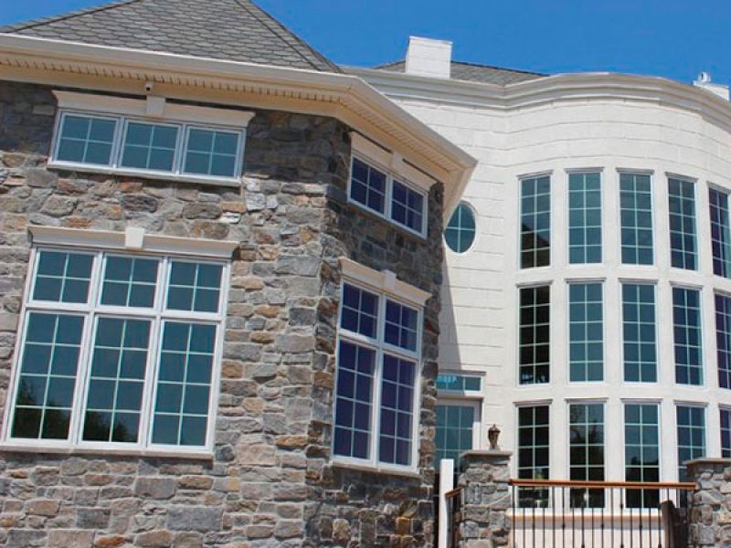 Stone and stucco house with large white-framed windows and a balcony. The QuarryCut logo is visible in the top left corner.